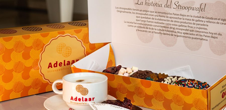 Cajas de regalo Adelaar abiertas, con stroopwafels y toppings junto a una taza de café